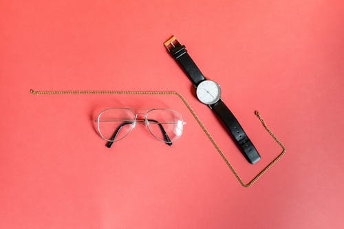 Free Gold-colored Necklace in Between Analog Watch and Eyeglasses on Pink Surface Stock Photo