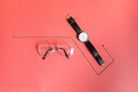 粉红色背景上，眼镜、手表和金项链的特写