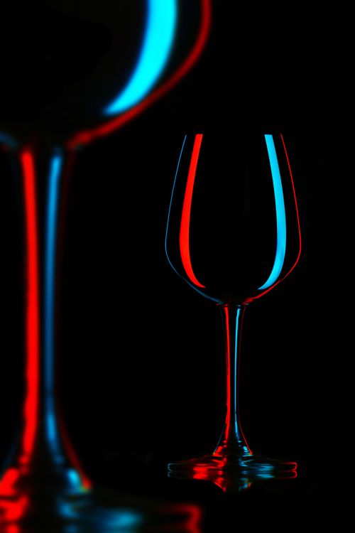 Free Artistic shot of wine glasses with striking neon red and blue light reflections on a black background. Stock Photo