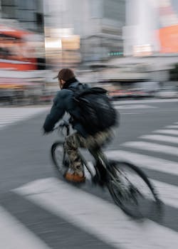 A person bicycling swiftly across a crosswalk in bustling Tokyo, Japan.