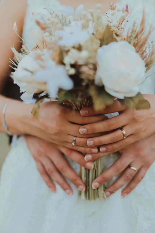 Free Close-up of a couple holding a wedding bouquet, showcasing rings and romance. Stock Photo