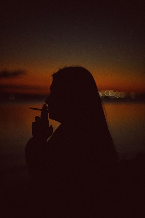 Free Artistic silhouette of a person smoking against a vibrant twilight background over water. Stock Photo