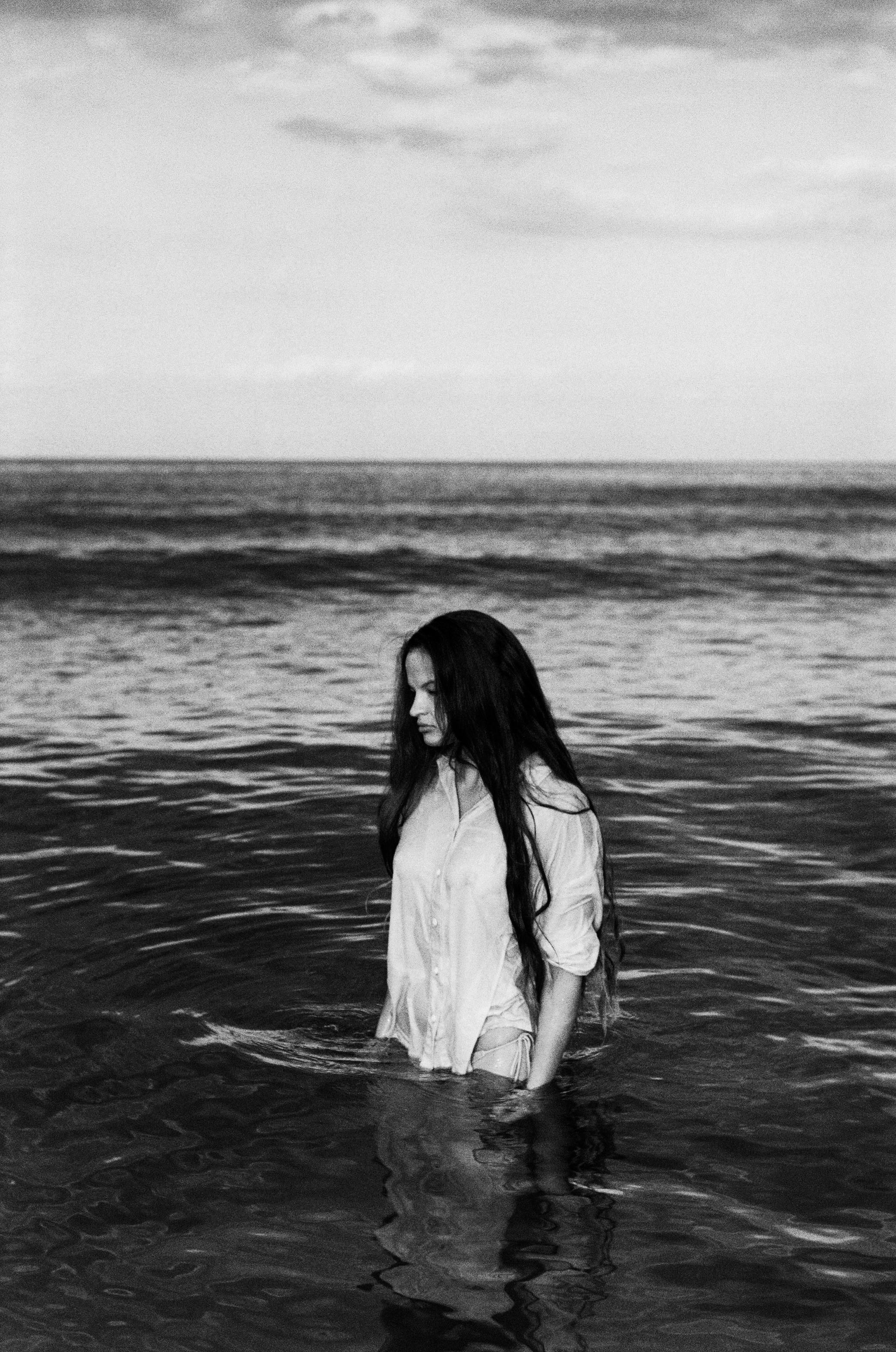 Woman wading in ocean with long hair and white shirt in Greece.