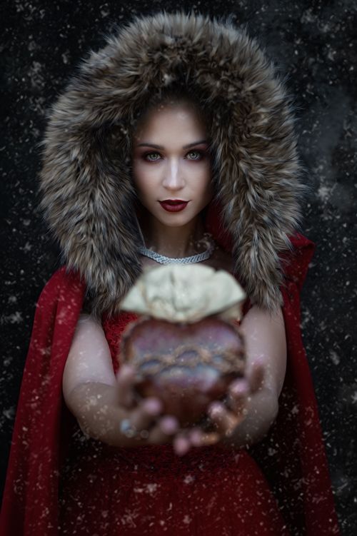 Free A mysterious woman in a fur-lined red cloak offering a heart during a snowstorm. Stock Photo