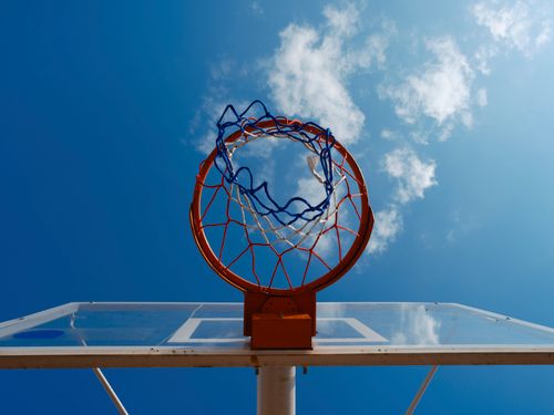 Free Basketball hoop captured from below with clear blue sky and clouds, ideal for sports themes. Stock Photo
