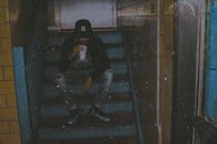 一名男子坐在城市昏暗光线的楼梯上，用纸杯喝水