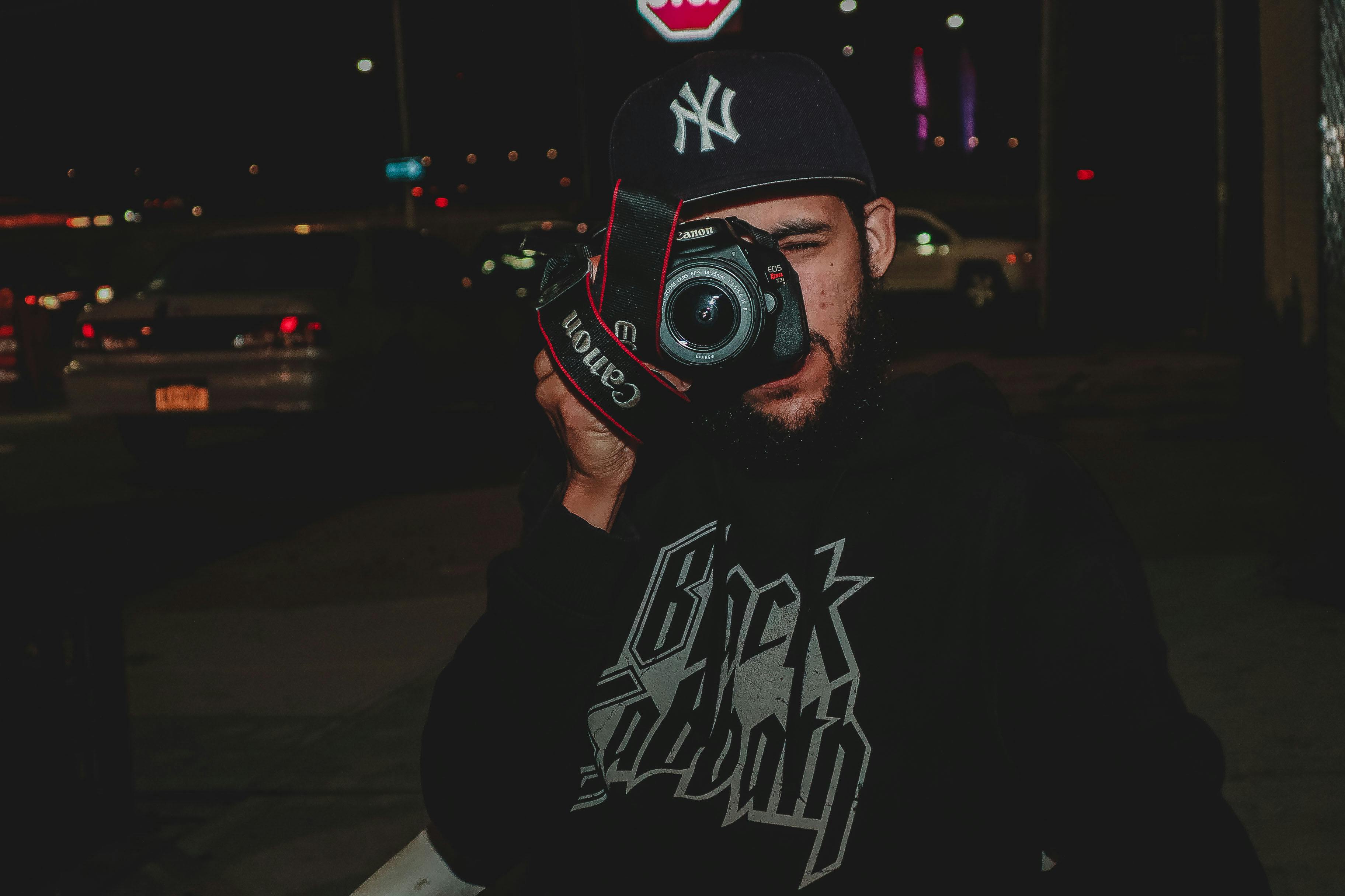 Bearded man with a DSLR camera capturing a night street scene outdoors.