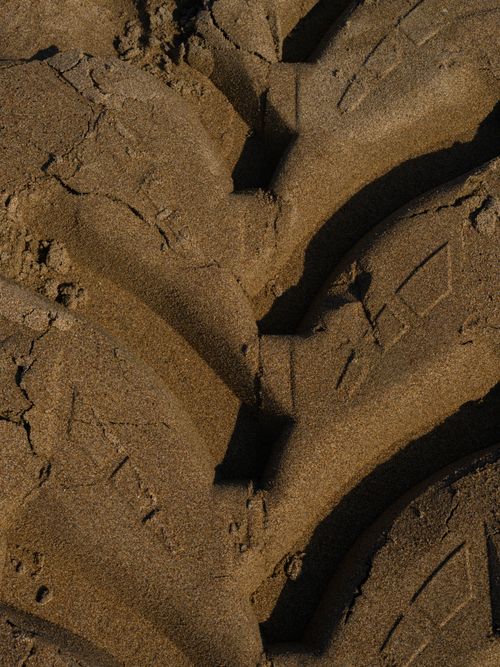 Free Detailed view of tire tracks imprinted in sandy ground under bright sunlight. Stock Photo
