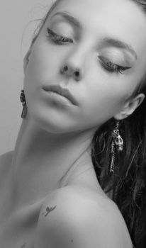 Striking black and white studio portrait of a young woman with dramatic makeup and earrings.