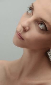 Close-up portrait of a woman looking upwards with subtle makeup and neutral background.