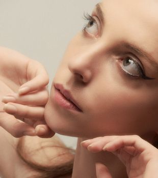 Close-up portrait of a woman with elegant makeup, posing with hands on face.