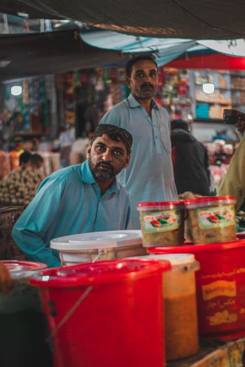 Free Two vendors in a bustling street market with colorful containers and spices in focus. Stock Photo