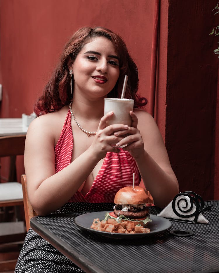 Smiling Woman Eating Burger At Cafe Table