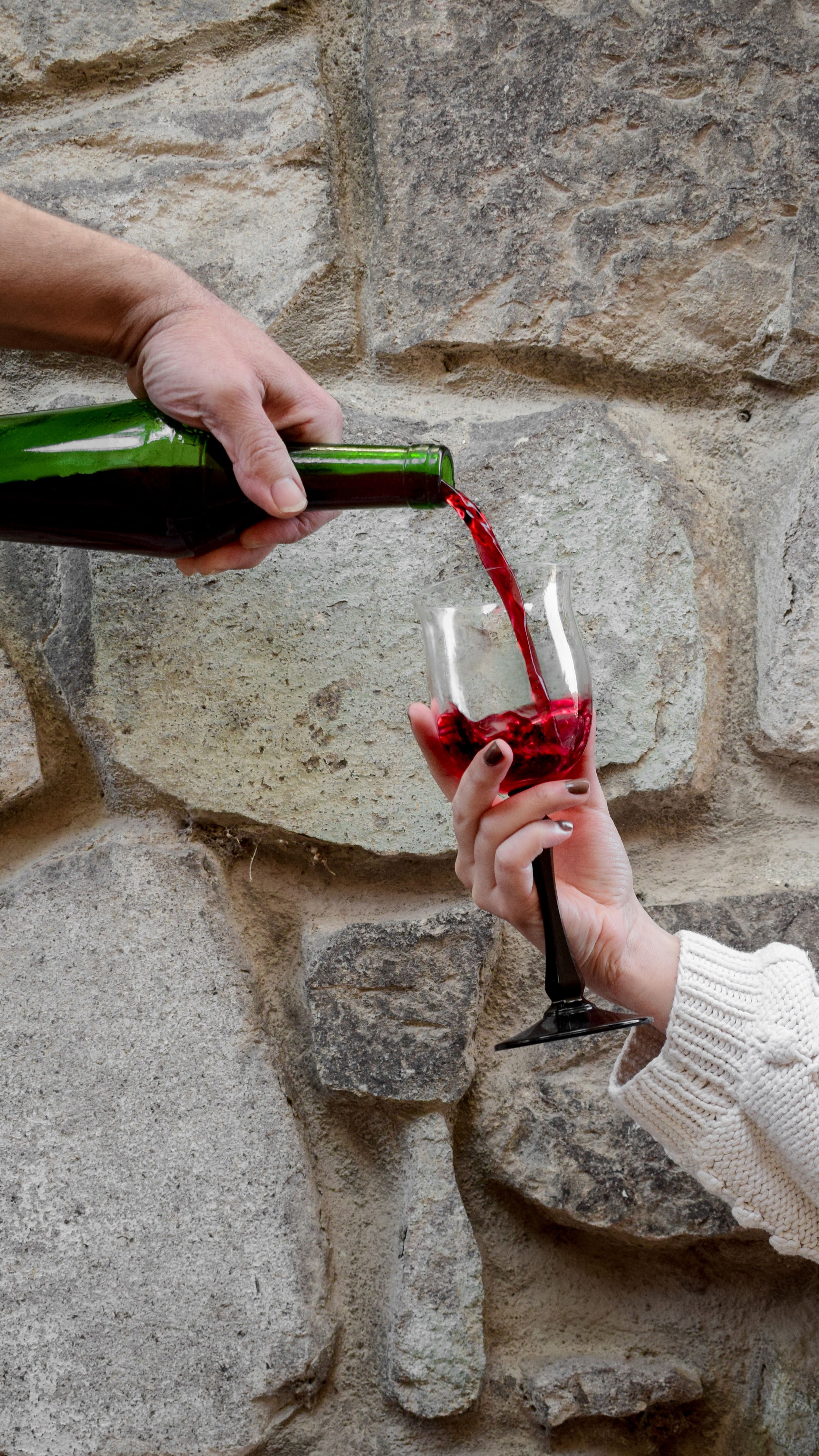 Red wine poured into a glass against a stone wall