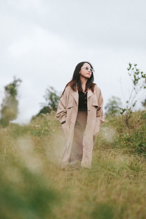 Free A fashionable woman posing in a meadow wearing a beige coat and sunglasses. Stock Photo