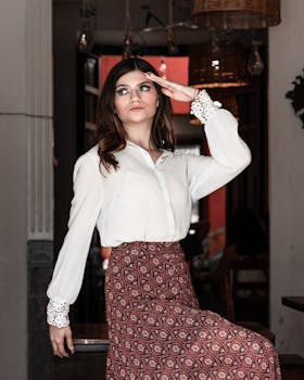 Stylish woman in white blouse posing elegantly indoors against decorative background.