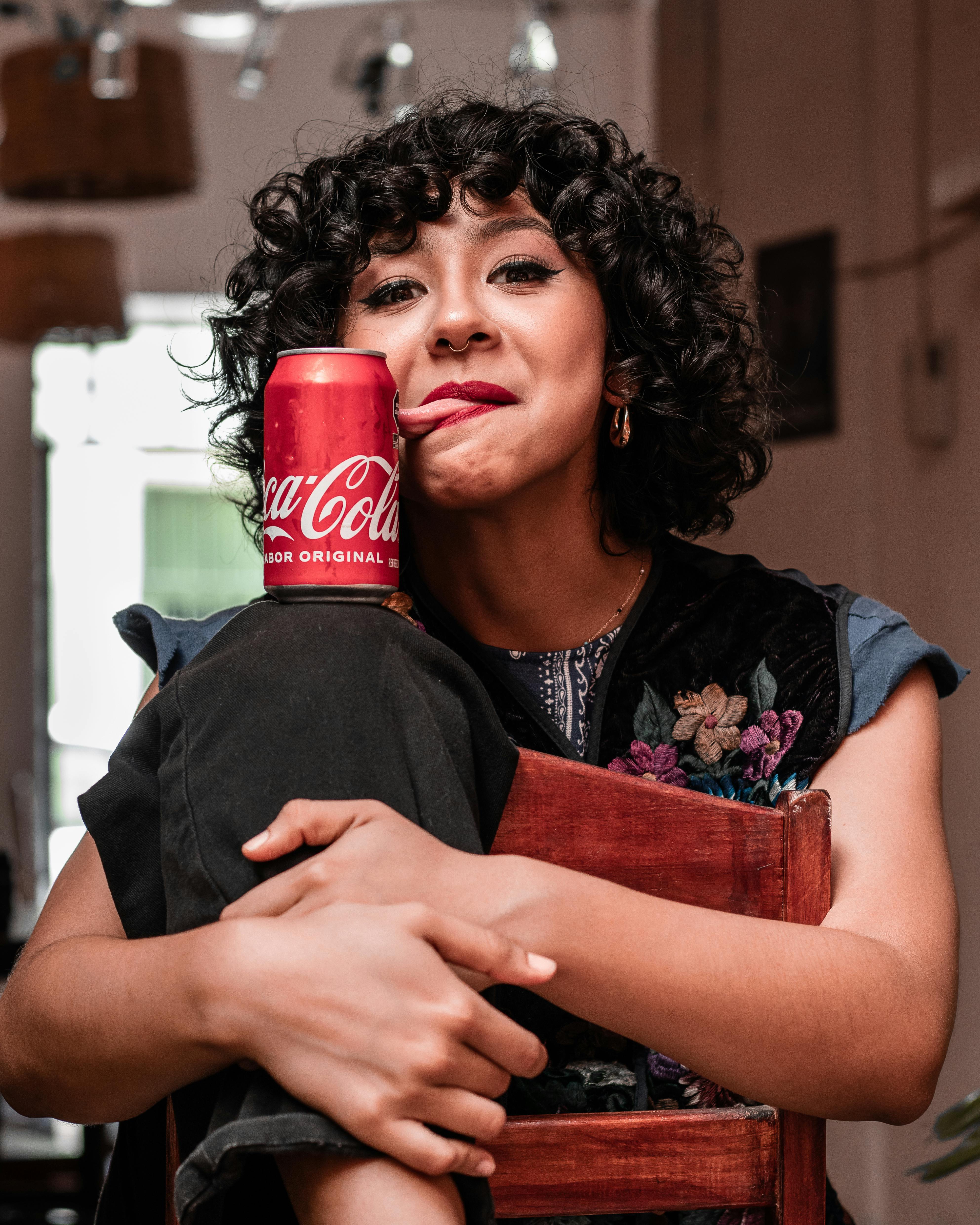 Charming brunette smiling and holding a Coca-Cola can indoors.