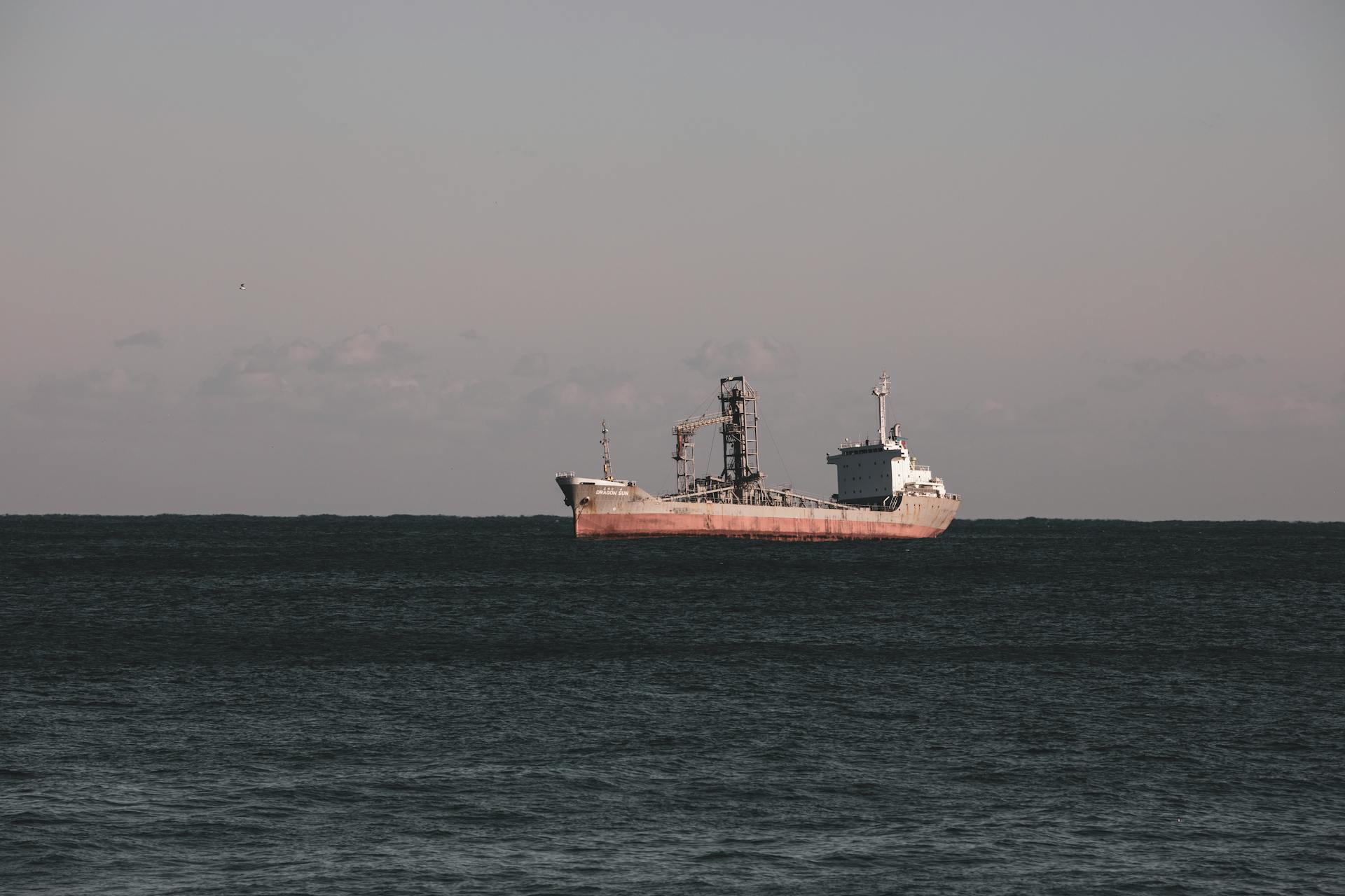 A lone cargo ship sails the tranquil waters of Donghae, South Korea under a pastel sky.