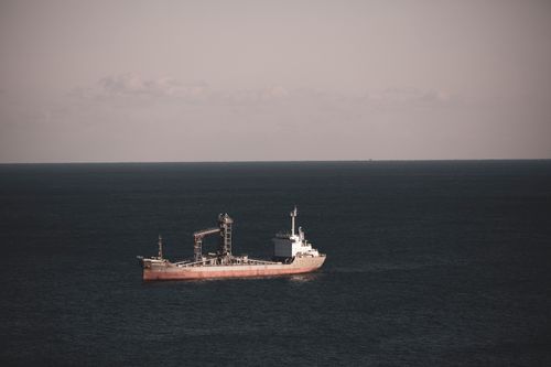 Free A lone cargo ship cruising through the vast and tranquil open sea under a pastel sky. Stock Photo