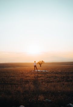 A solitary person stands on a vast field under a dramatic sunset sky, evoking a sense of tranquility.