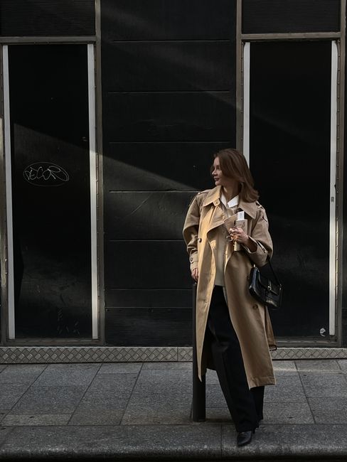 Stylish woman in a trench coat standing on a Paris street, exuding elegance and urban fashion.