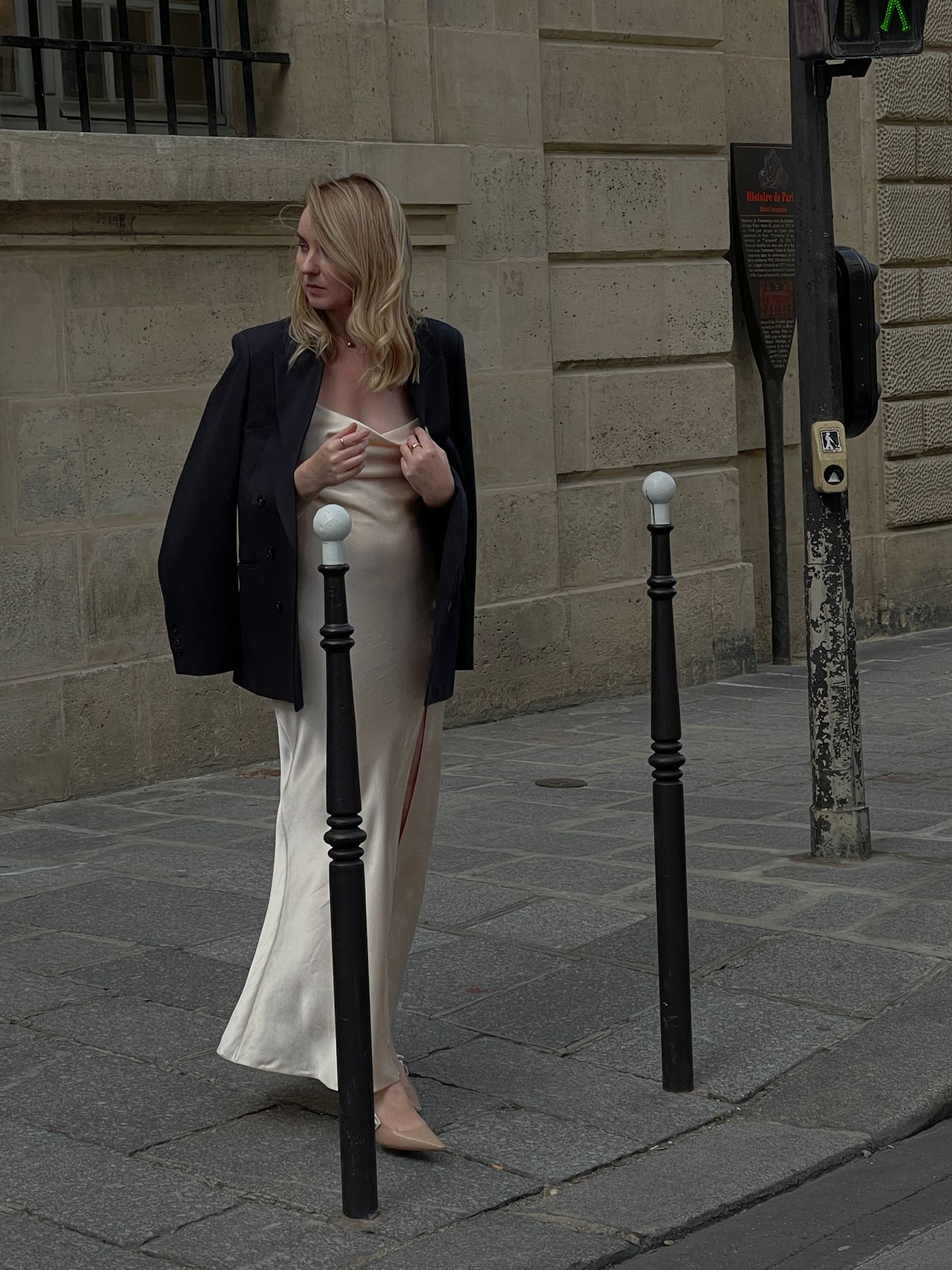 A woman in a long evening dress and black blazer standing on a sidewalk — the slip and blazer formula