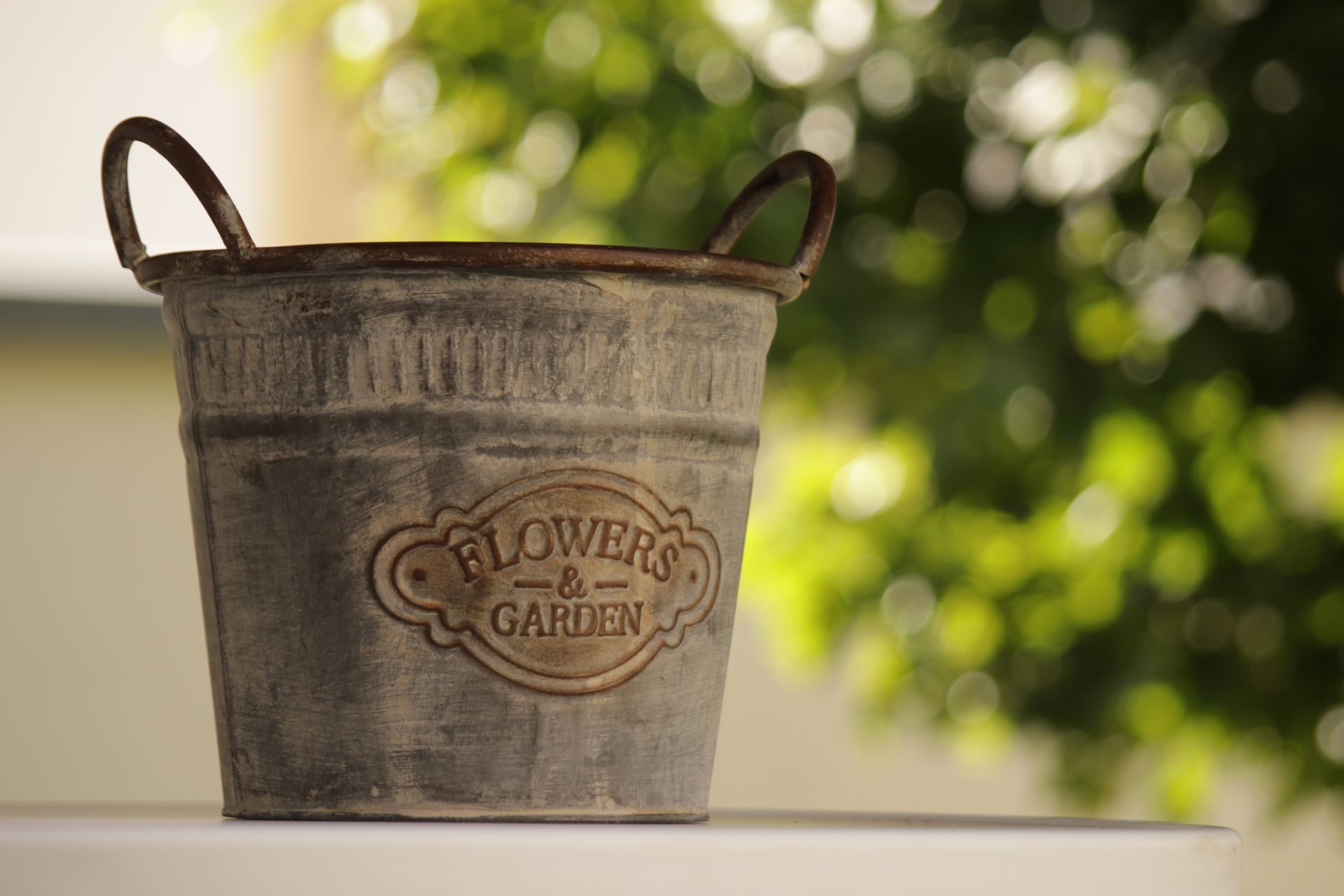 Close-up of a rustic garden bucket with 'Flowers & Garden' text against a blurred green background.