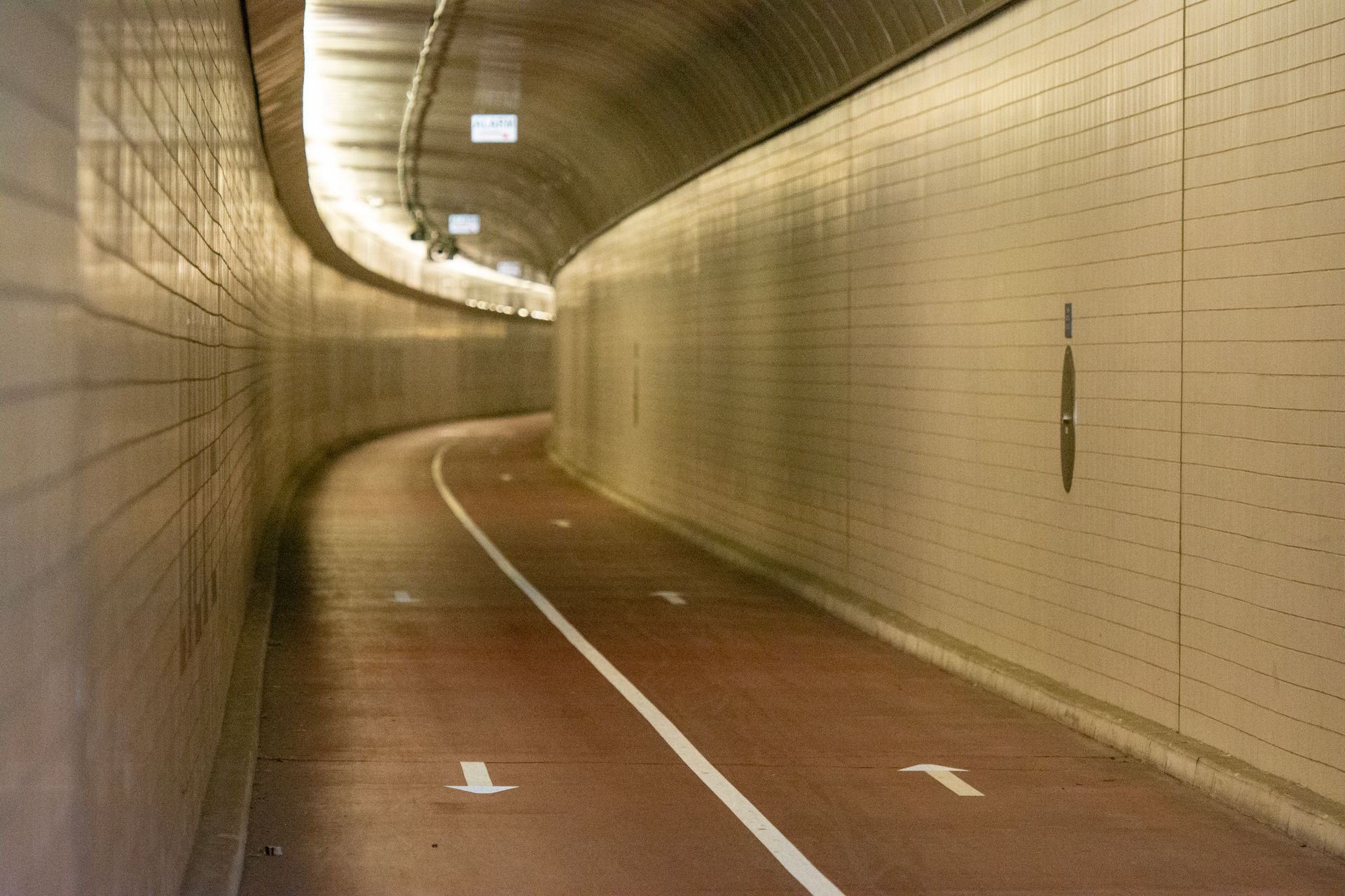 A well-lit curved tunnel with a bicycle lane and directional arrows on the floor.