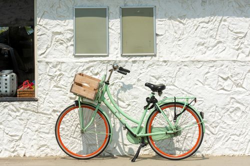 Free A stylish mint green bicycle with an orange rim parked against a textured white wall in sunlight. Stock Photo