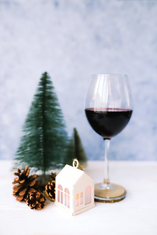 Free A cozy winter arrangement featuring a wine glass, pinecones, decorative house, and mini Christmas trees. Stock Photo