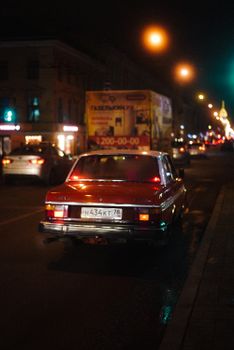 A classic red car captured on a bustling city street during the nighttime.