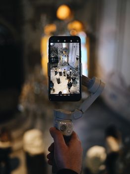 Hand holding a smartphone on a gimbal, capturing a grand interior scene.