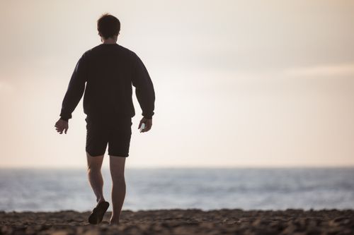 Free A man walking alone on a beach by the sea, capturing a serene, contemplative moment. Stock Photo