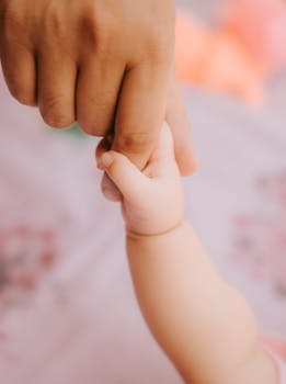 A close-up shot of a baby's delicate hand softly holding an adult's finger, symbolizing connection and care.