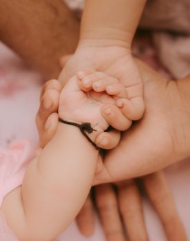 Close-up of a baby's hand gently held by an adult, symbolizing care and connection.