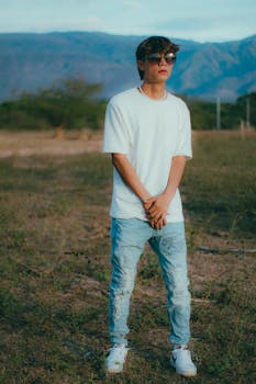Teenager standing in a rural Colombian landscape wearing casual fashion with sunglasses.