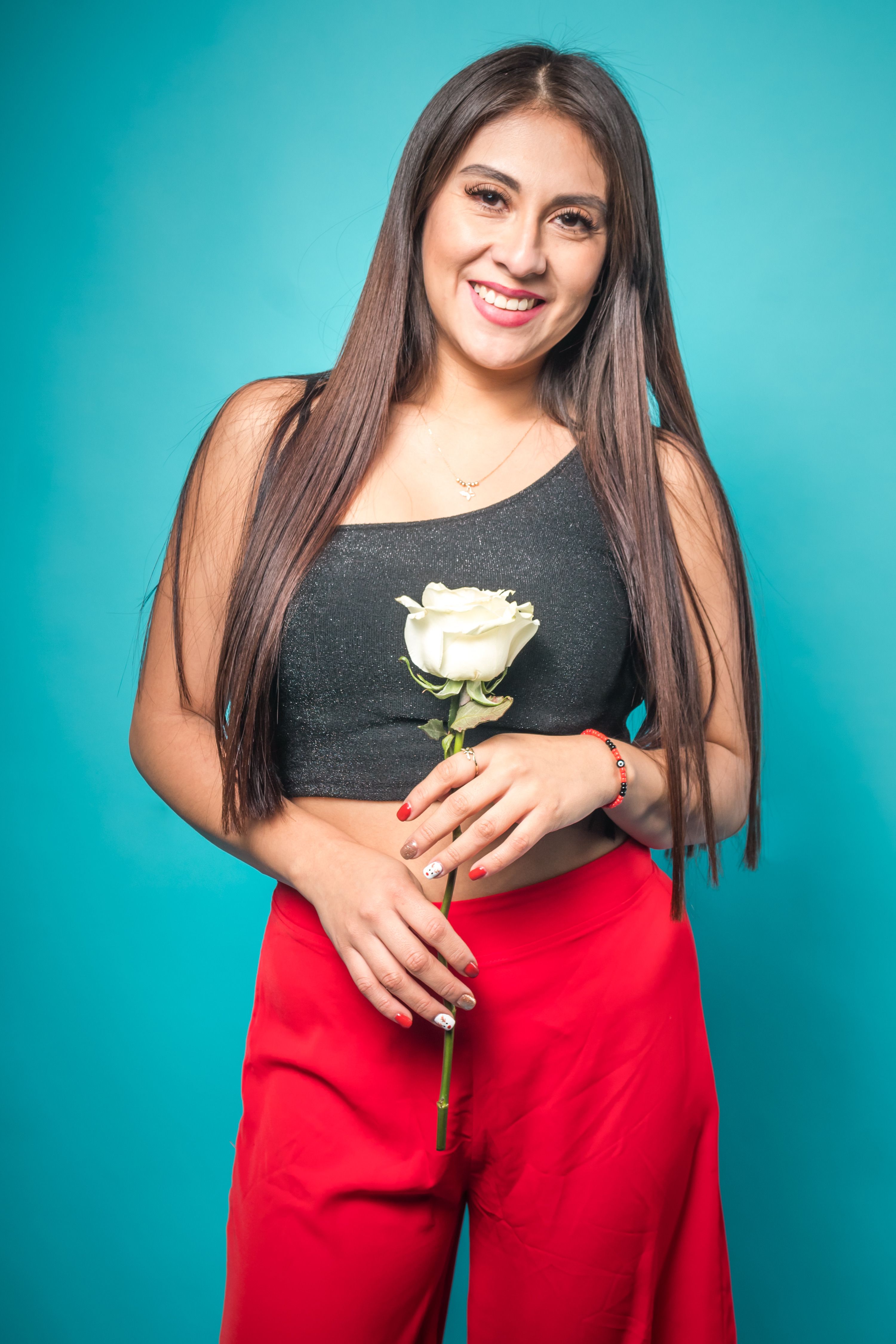 Happy woman in casual attire holding a white rose against a blue background in studio.