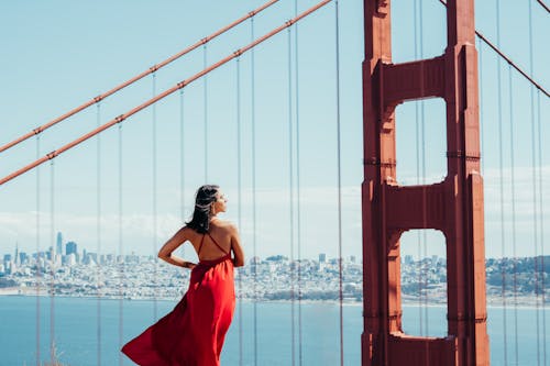 Woman in Red Dress Standing Near Orange Bridge