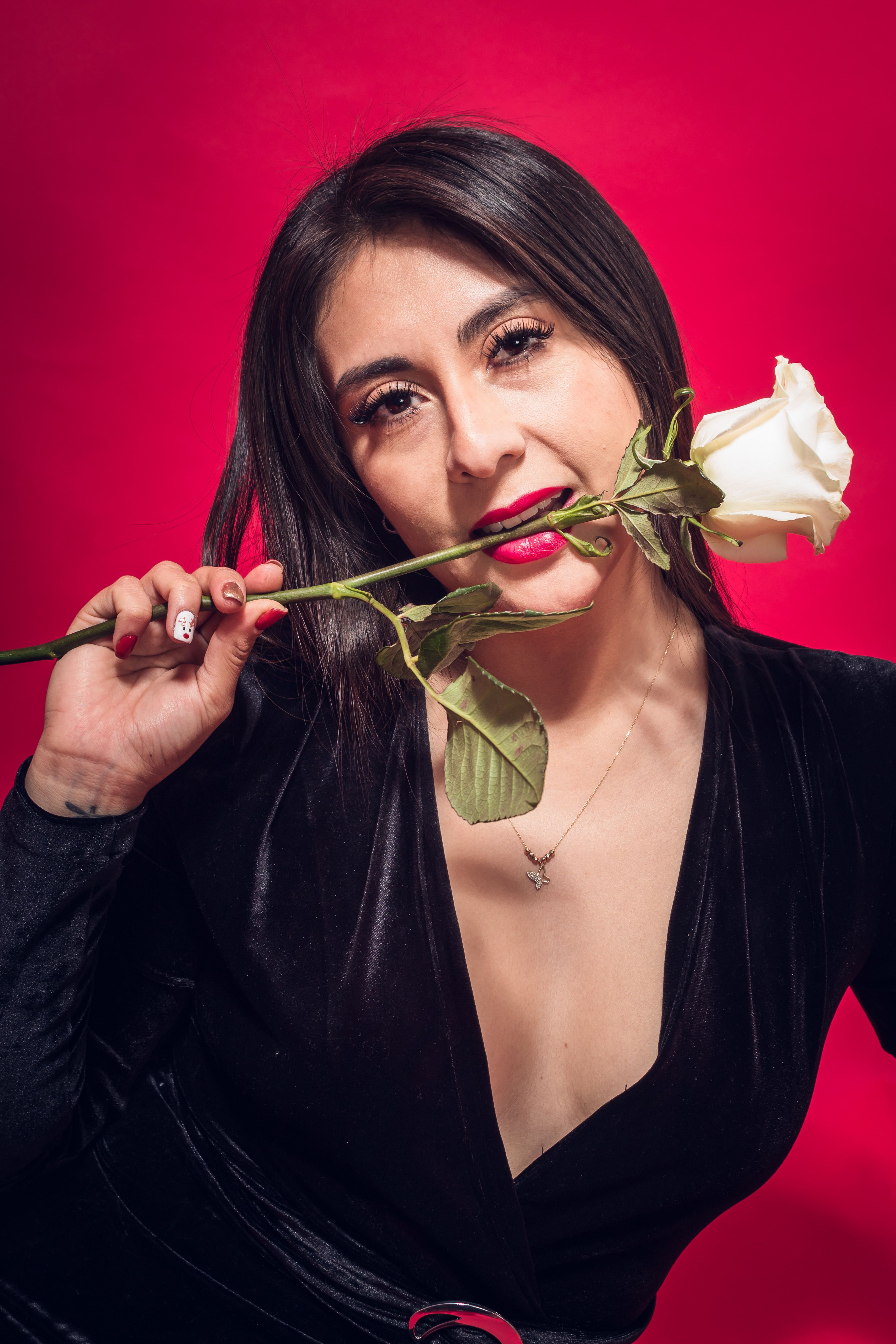 Portrait of a brunette woman with a white rose against a vibrant red background.