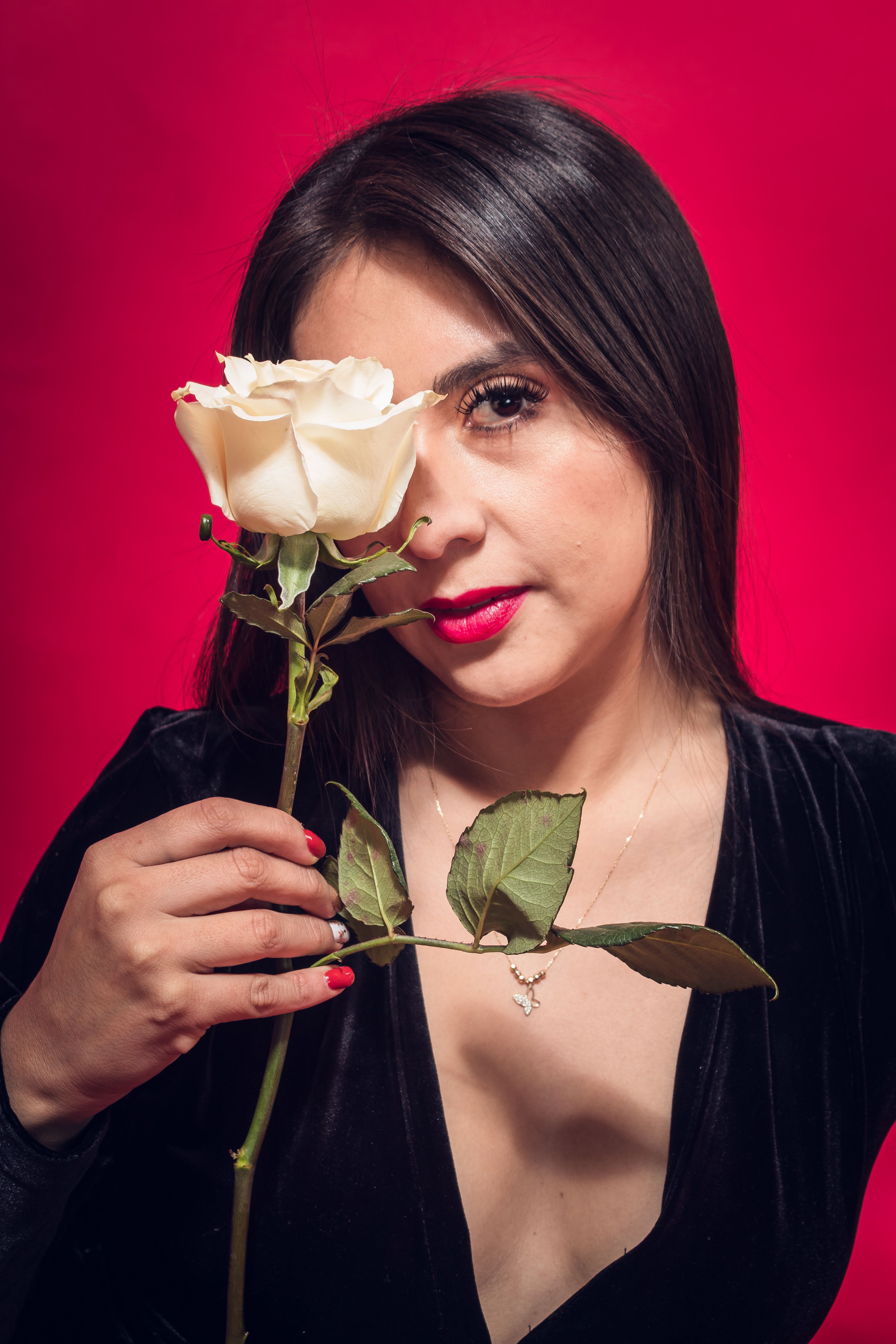 A woman in a black dress holds a white rose against a bold red background.