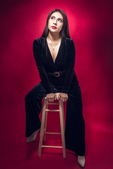 Stylish portrait of a woman in black on a stool with a vibrant red backdrop.