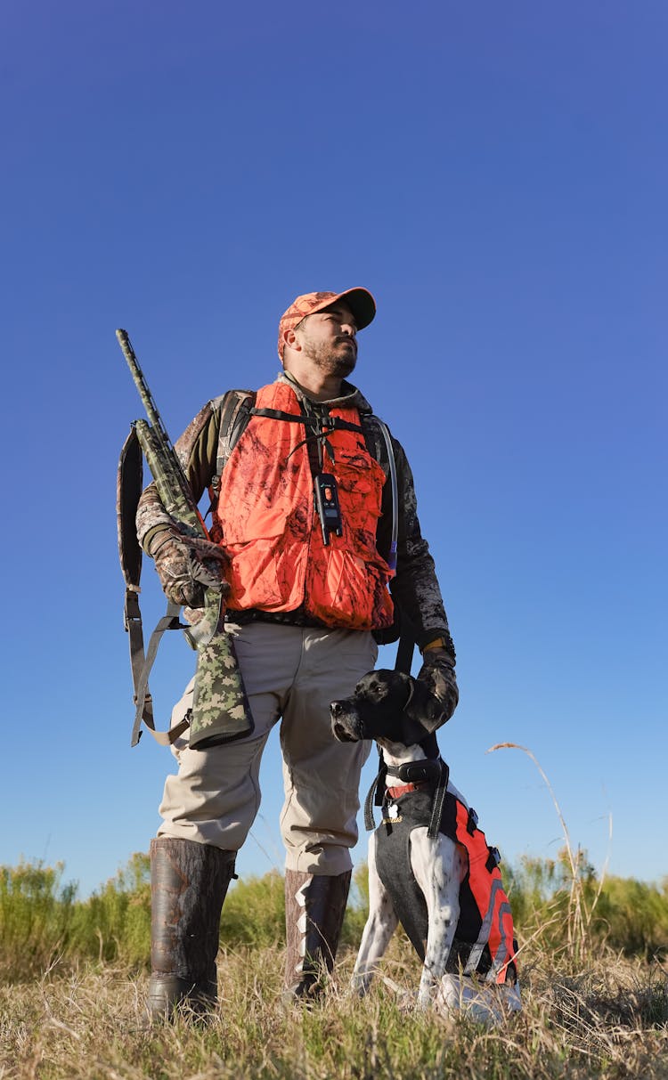 Low Angle Shot Of A Man With A Dog And Weapon, On A Field