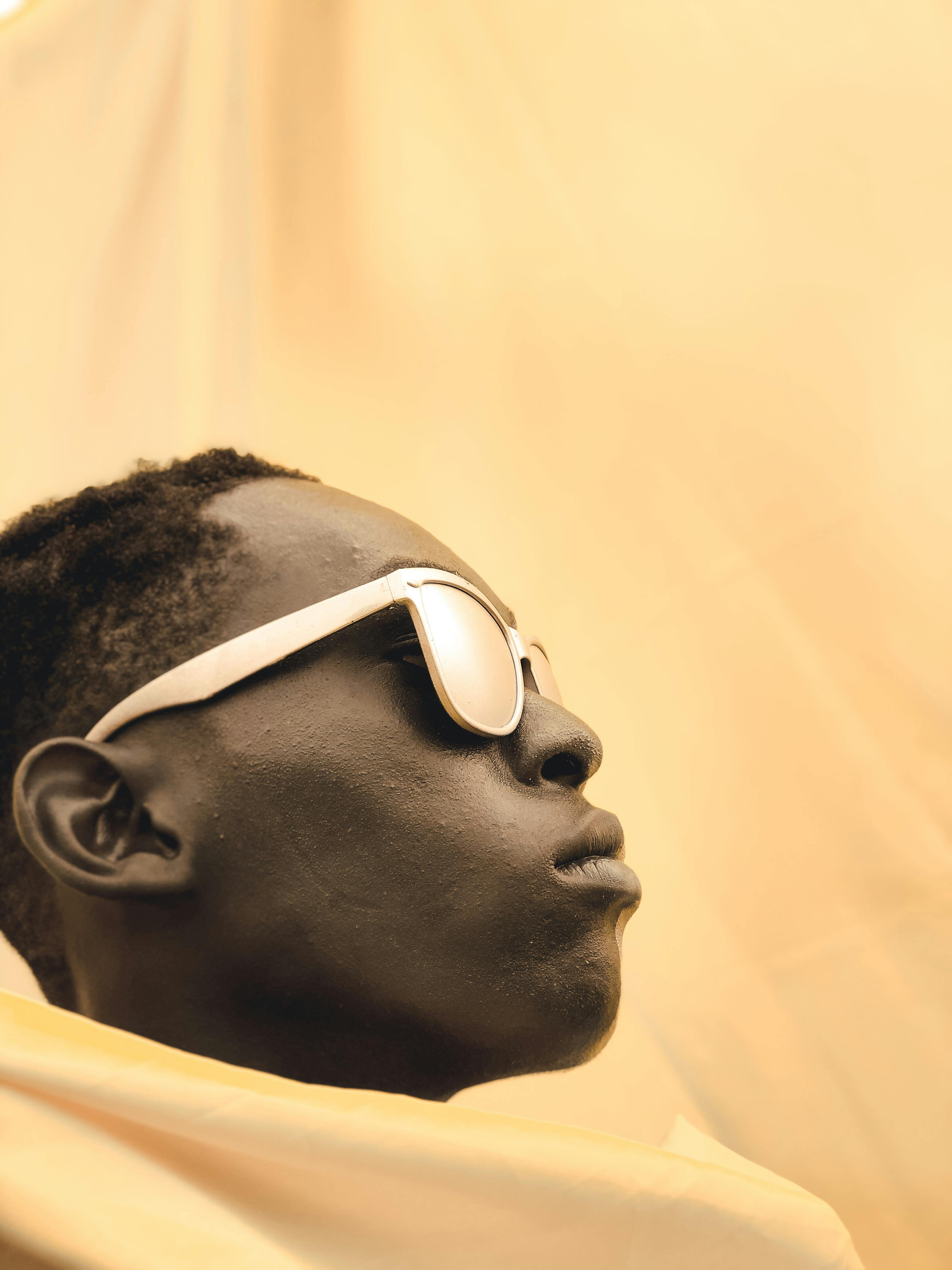 Artistic side profile portrait of a person wearing sunglasses with warm yellow tones.