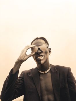 A sepia-toned image of a stylish young man adjusting his sunglasses, showcasing modern fashion and attitude.