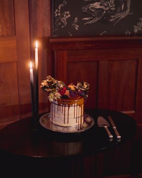 A stylish wedding cake adorned with fruit and flowers, lit by candles in an elegant indoor setting.