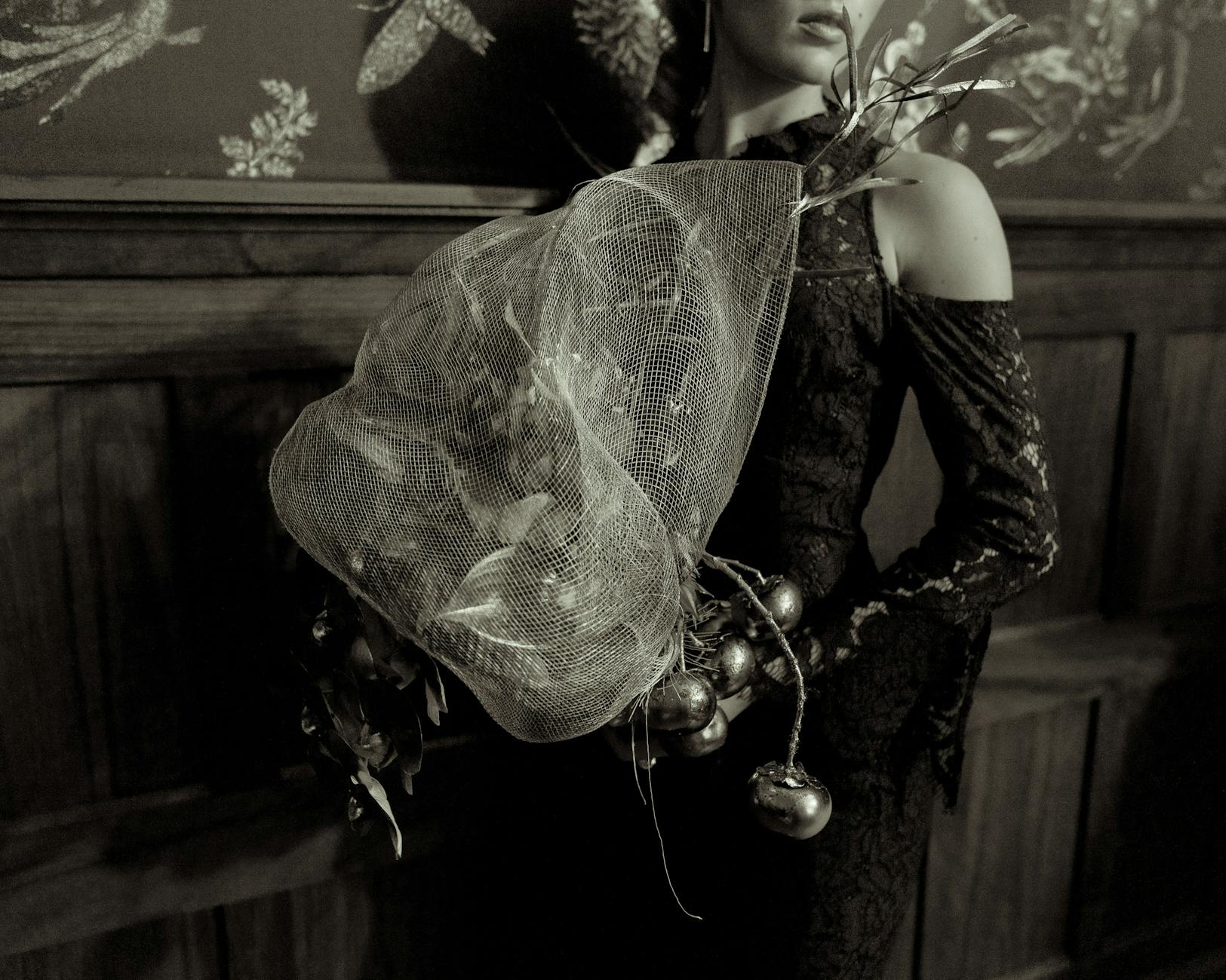 Sepia-toned portrait of a woman holding an ornate bouquet in a vintage elegant setting.