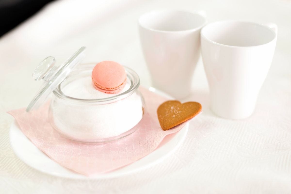 A delicate tea setup featuring a jar of sugar, macaron, heart cookie, and two cups on a soft background.