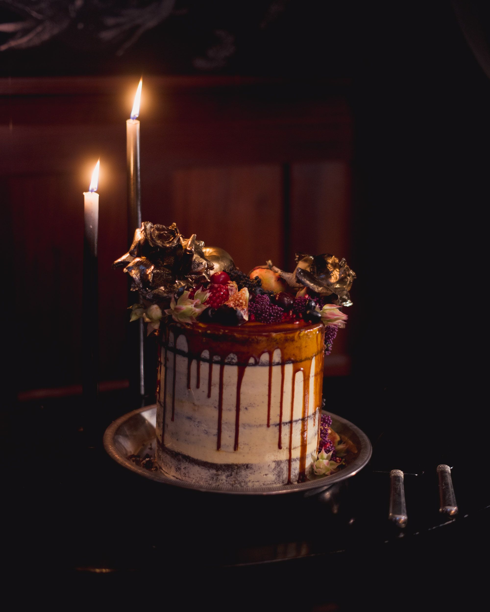 Luxurious drip cake adorned with berries, lit by glowing candles in a dark setting.