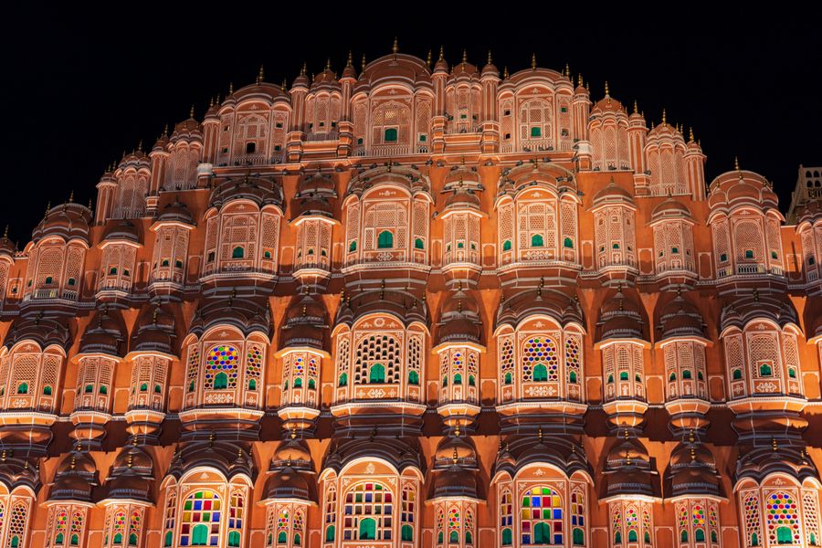 The iconic Hawa Mahal's illuminated facade in Jaipur, showcasing intricate architecture and vibrant colors.