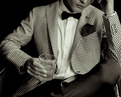 A man in a suit and bow tie holding a drink